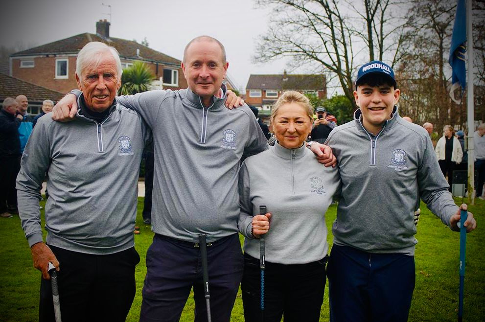 Three men standing on a golf green, the club captain and former captain flanking a prize winner holding a trophy.