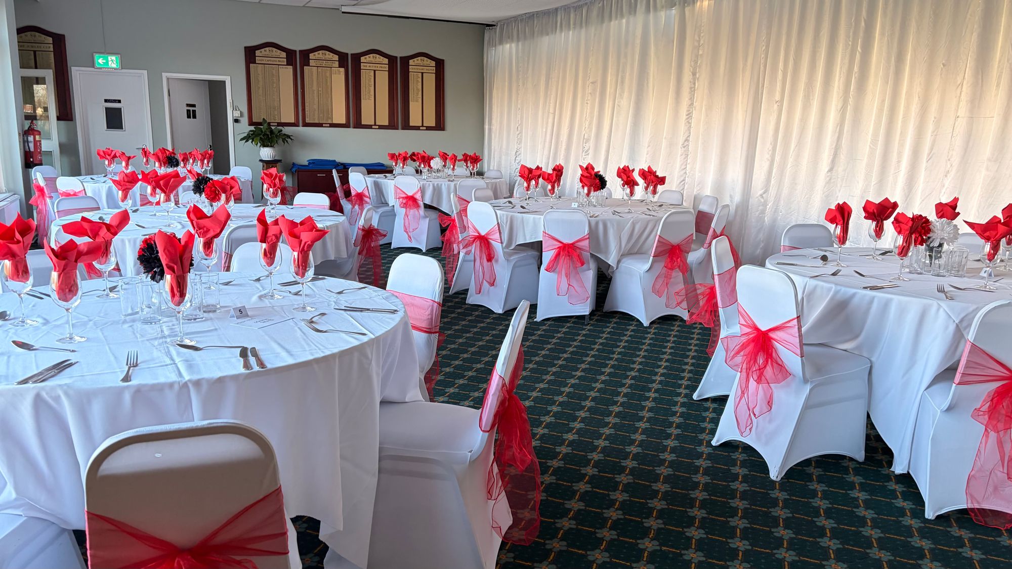 Group of people seated around banquet tables with pink and orange napkins, a centerpiece of pink flowers, and warm string lights in the background.